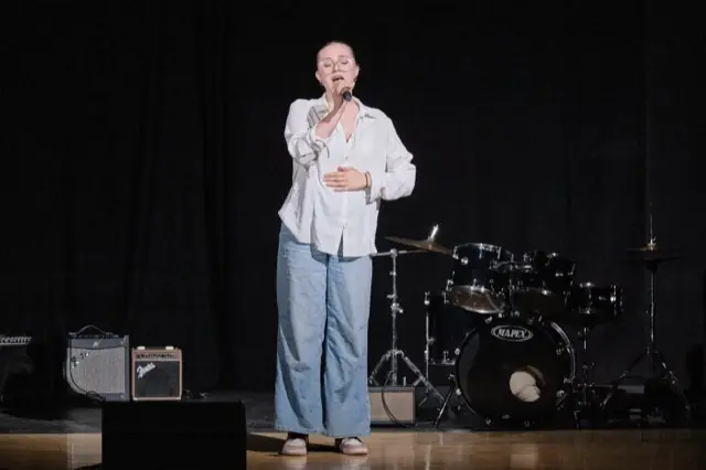 Wokalistka z mikrofonem na scenie auli salezjańskiej, koncert charytatywny 2025